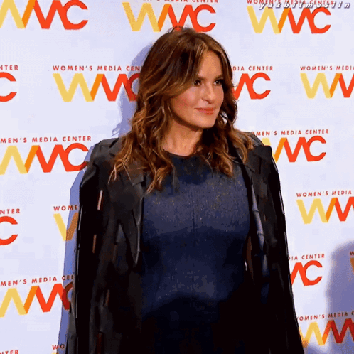Woman in Blue Dress in Front of Wall Saying Women's Media Center