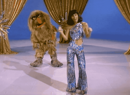 Woman in Blue Jumpsuit Dancing Next to Sesame Street Character