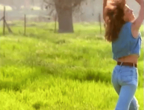 Woman In Blue Shirt And Jeans Standing In Grass Field GIF