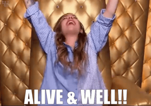 Woman in Blue Shirt Arms in Air Alive & Well