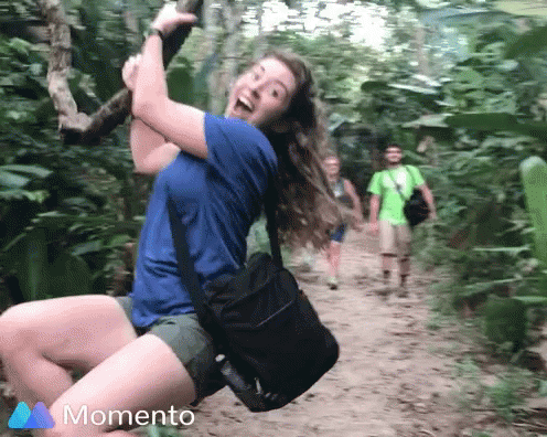 Woman In Blue Shirt Swinging On Rope In Woods With Momento Logo GIF