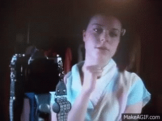 Woman in Blue Shirt with Hands Up in Dark Room