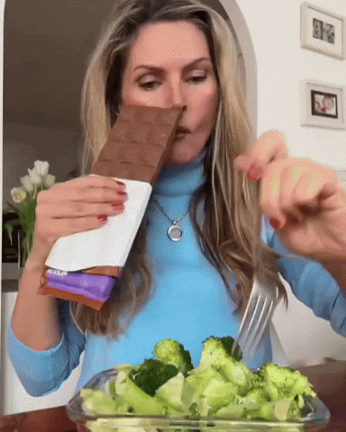 Woman in Blue Sweater Eating Broccoli and Milka Chocolate
