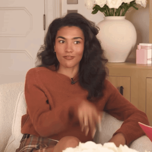 Woman In Brown Sweater Sitting On Couch With Flowers GIF