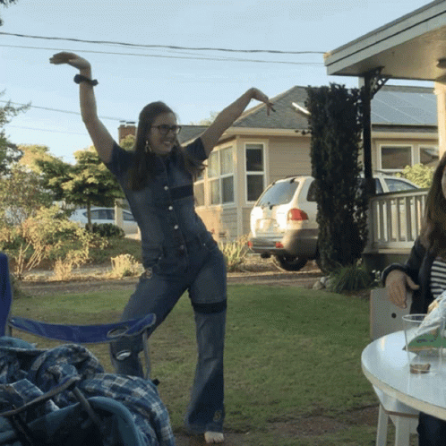 Woman In Denim Jumpsuit With Arms Up Outside House GIF