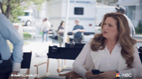 Woman in Director's Chair Holding Cell Phone With NBC Logo