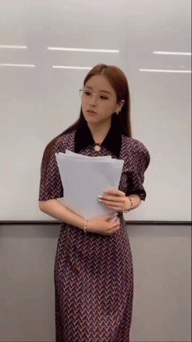 Woman In Dress Holding Paper In Front Of White Board GIF