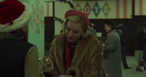 Woman in Fur Coat Talks to Man in Santa Hat Toys Sign