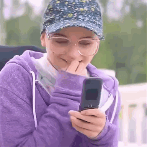 Woman In Glasses And Hat Laughing On Flip Phone GIF