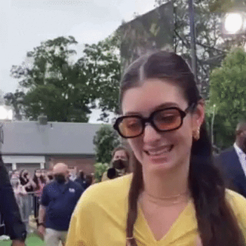 Woman In Glasses And Yellow Shirt Smiling At Crowd GIF