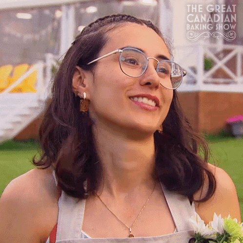 Woman In Glasses Smiling In Front Of The Great Canadian Baking Show Sign GIF