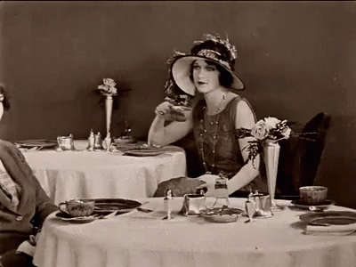 Woman In Hat Sitting At Table With Plates And Cups GIF