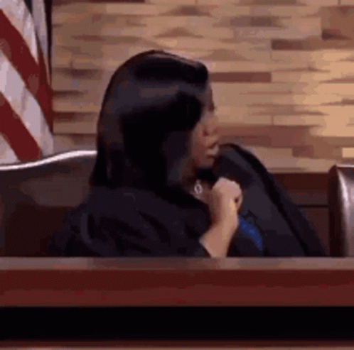 Woman In Judge Robe Sitting At Table In Front Of American Flag GIF