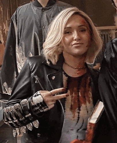 Woman In Leather Jacket Giving Peace Sign Holding Book GIF