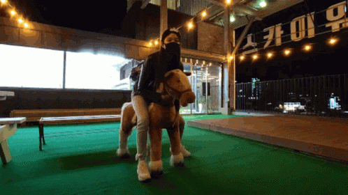 Woman in Mask Riding Stuffed Horse in Front of No Sign
