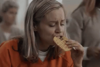 Woman in Orange Shirt Eating Waffle in Jail Cell