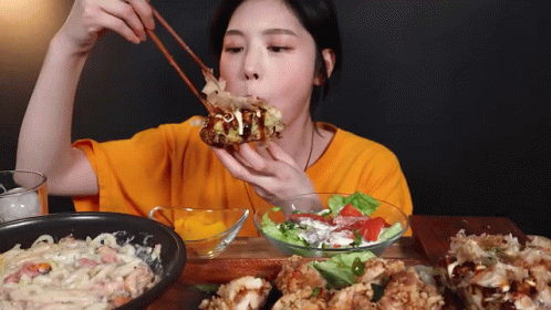 Woman in Orange Shirt Eating with Chopsticks