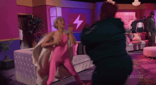 Woman in Pink Bodysuit Fighting Man in Green Jacket in Front of Zeusz Sign