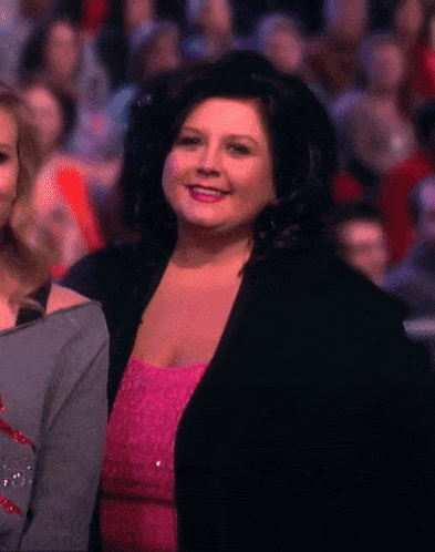 Woman in Pink Dress and Black Jacket Smiling Before Crowd