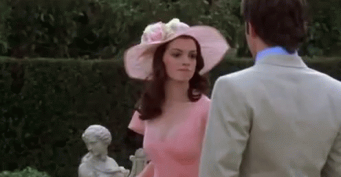 Woman in Pink Dress and Hat Next to Man in Suit
