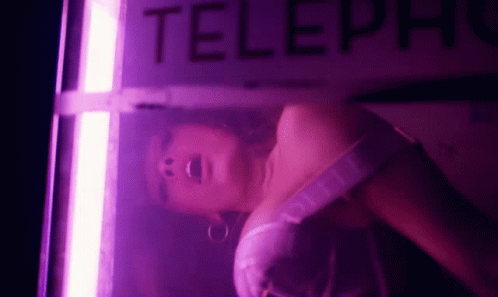 Woman in Pink Dress Laying in Telephone Booth With Purple Light
