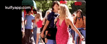 Woman In Pink Dress Next To Man In Blue Shirt In Front Of Crowd GIF