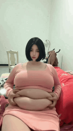 Woman in Pink Dress Sitting on Bed Hands on Stomach
