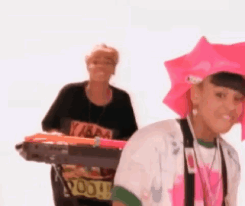 Woman in Pink Hat Holding Umbrella Next to Woman With Keyboard
