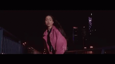 Woman in Pink Jacket Dancing on Bridge at Night