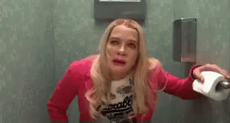 Woman In Pink Jacket Holding Toilet Paper In Public Restroom GIF