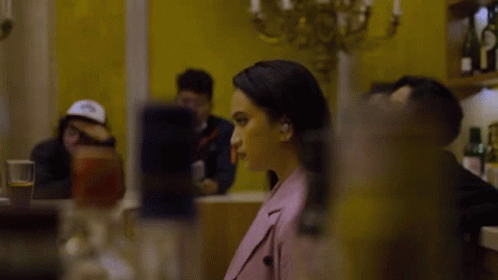 Woman in Pink Jacket Sitting at Table in Front of Yellow Wall