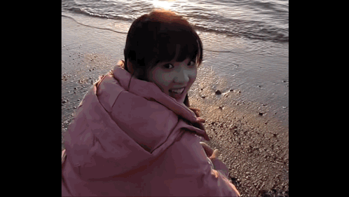 Woman In Pink Jacket Standing On Beach GIF
