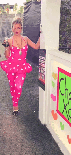 Woman In Pink Polka Dot Outfit Standing In Front Of Cha Xoxo Sign GIF