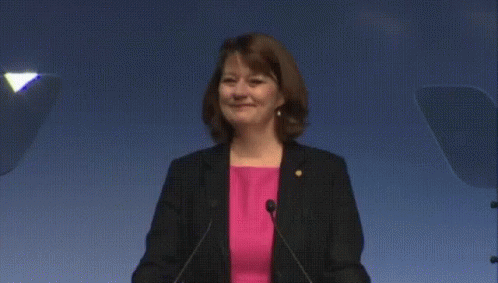 Woman in Pink Shirt and Black Jacket at Podium With Microphones
