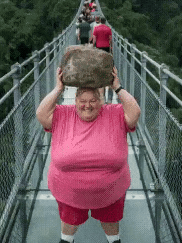 Woman in Pink Shirt Carrying Rock on Bridge