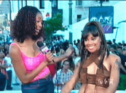 Woman In Pink Tank Top Talking Into Microphone Next To Another Woman GIF