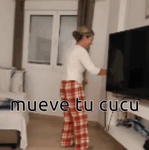 Woman in Plaid Pants Standing Before TV Saying Mueve Tu Cucu