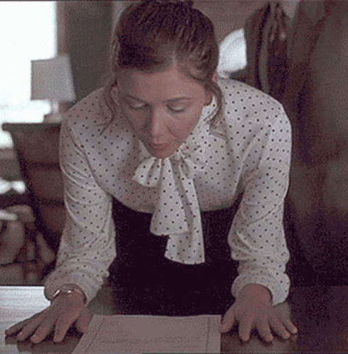 Woman In Polka Dot Blouse Kneeling At Desk Looking At Paper GIF