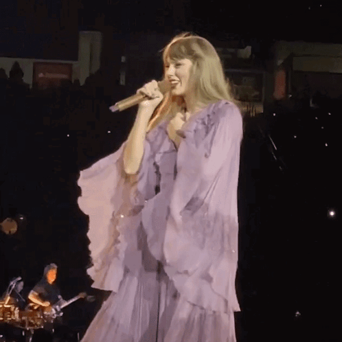 Woman in Purple Dress Singing Into Microphone on Stage