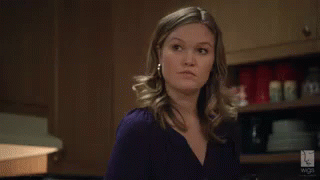 Woman In Purple Shirt And Earrings Standing In Kitchen GIF