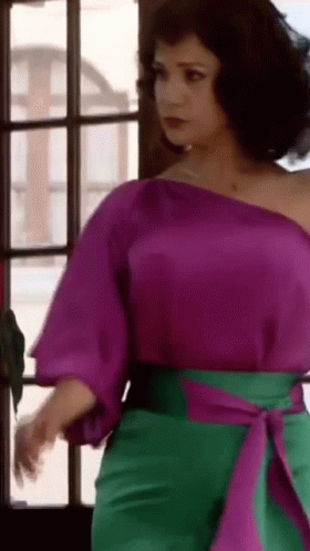Woman in Purple Top and Green Pants Standing by Window