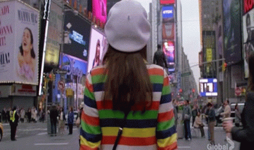 Woman In Rainbow Striped Jacket And White Hat Walking GIF