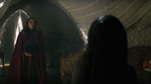 Woman in Red Cape Talking to Woman in Dark Room
