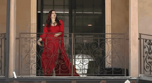 Woman In Red Dress On Balcony With Wrought Iron Railing GIF