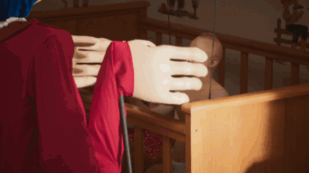 Woman in Red Dress Standing in Room With Dresser and Crib