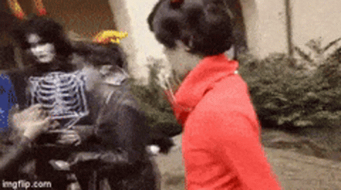 Woman In Red Jacket Next To Skeleton Costume GIF