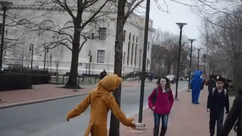 Woman In Red Jacket Walking With Man In Bear Costume Behind GIF