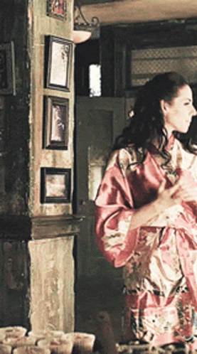 Woman in Red Robe Standing Before Wall of Pictures