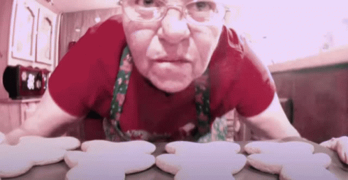 Woman In Red Shirt And Apron Looking At Gingerbread Cookies GIF
