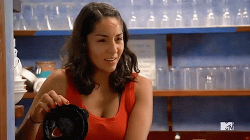 Woman In Red Tank Top Smiling In Front Of MTV Shelf GIF